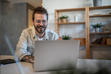 Smiling freelancer working from home using laptop and holding pen