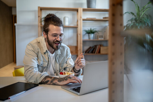 Freelancer eating breakfast and working on laptop at home