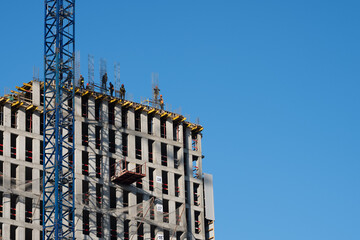 Construction workers are working on top of a concrete building under construction with a crane and blue sky
