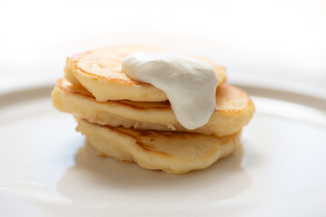 Delicious pancakes stacked on a white plate with cream cheese dripping on them, ready to be eaten for breakfast
