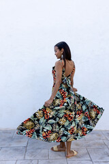 Woman in summer colored dress posing on a white wall.