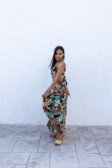 Woman in summer colored dress posing on a white wall.