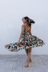 Woman in summer colored dress posing on a white wall.