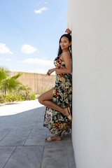 Woman in summer colored dress posing on a white wall.