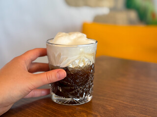 Glass of Freddo Cappuccino Greek iced coffee drink with espresso and cold frothy milk in female hand close up