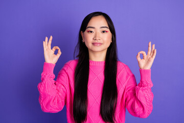 Portrait of a stylish young woman in pink sweater against purple background, expressing positivity...