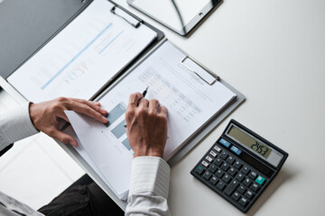 Male office staff analyzing accounting paperwork during financial review with attention to...
