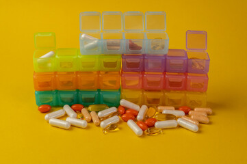 Heap of different pills scattered in front of colorful medicine organizers on yellow background....