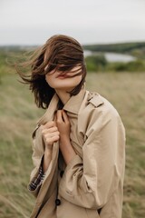Model pulling trench coat together in windy field during photoshoot