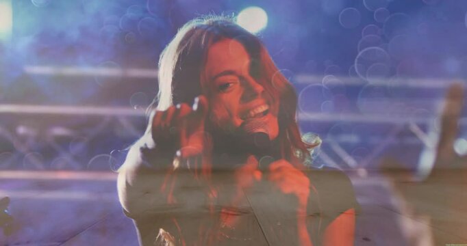 Female singer stepping into spotlights on music stage, singing into mic and pointing to engage fans