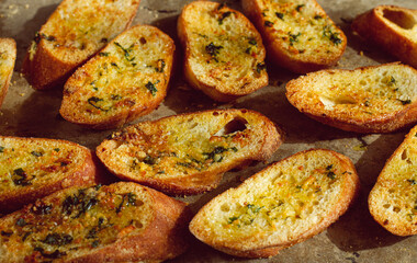 baguette toasts, baked in the oven, with garlic butter and herbs, homemade, on a platter, top view,