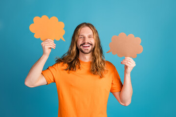 Happy young man in casual attire holding colorful thought cloud props against a bold blue background