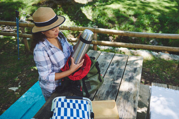 Woman Preparing Picnic at a Park Bench with Thermos and Backpack