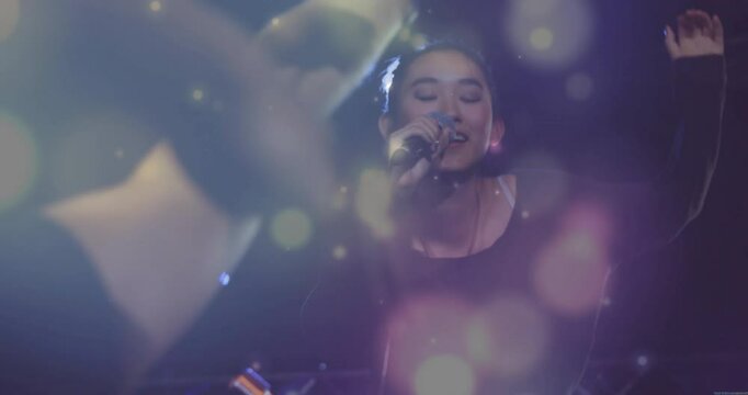 Singer stepping into spotlight, singing into mic while engaging concert audience with bokeh flares