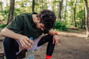 Tired athlete refreshing himself with water after intense workout in forest