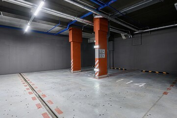 Indoor parking with orange columns, marked spaces, and visible ceiling pipes. Concrete floor and...