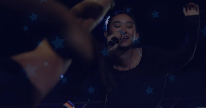 Concert singer with microphone raising arm starting verse, engaging fans reaching under star lights
