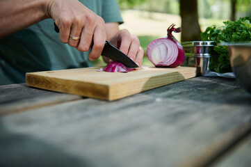 Person Cutting Red Onion on Wooden Board Outdoors in Bright Natural Setting