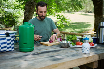 Man Preparing Vegetables Outdoors During a Scenic Picnic in Nature