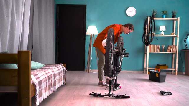 Woman repairing bicycle and fixing wheel with wrench at home.
