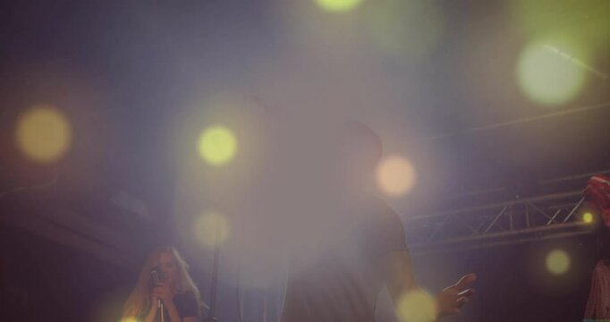 Lead singer stepping forward gripping mic singing while backing singers swaying under concert haze