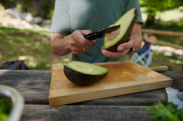 Hand Preparing Fresh Avocado Outdoors on Wooden Cutting Board