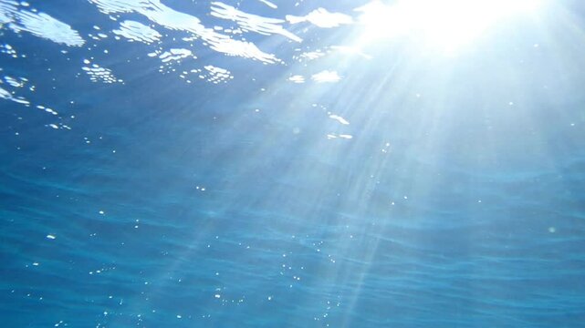 Light filtering down through blue water. Underwater sunlight in deep sea. Sunlight viewed from blue abyss, slow motion. Underwater sunlight shining deep under water with ripples on wave surface. sun.