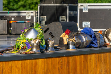 medieval knight armor elements on wooden stage with helmets, gauntlets and flower wreath, modern...