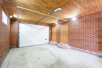 Interior of a garage featuring a white sectional door, brick walls, wooden ceiling, concrete floor...