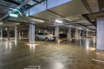 Indoor parking garage with concrete pillars, visible ductwork, and several parked cars. The floor...