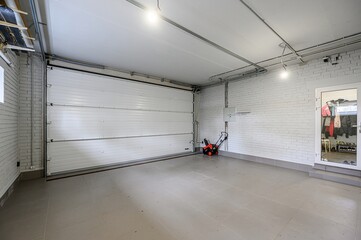 clean, bright garage with a partially open white door, gray tiled floor, and a snow blower....
