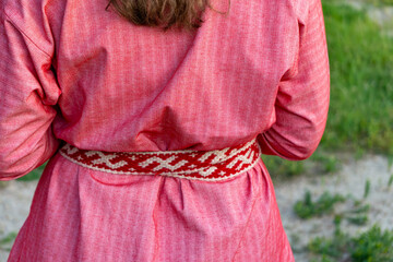 Rear view of a woman wearing a traditional red linen dress, tied with a handwoven woolen belt...
