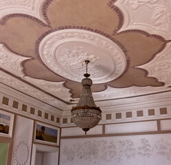 An ornate ceiling with a chandelier in a room with decorative wall panels and artwork.