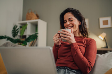 Woman enjoying hot beverage while working from home on laptop