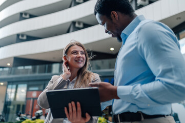 Business colleagues using tablet and discussing a project outside modern office building