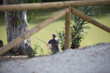 A lone fisherman on the river on a sunny summer day. Photo taken from behind.