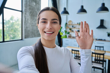 Close-up selfie portrait of teenage female looking waving hand at web camera