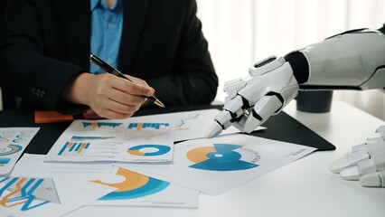 A human professional collaborates with a robotic hand in a modern office environment, analyzing...