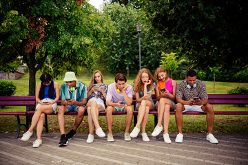 Young friends sitting on a park bench bonding over shared smartphone activities during a vibrant sunny day outdoors