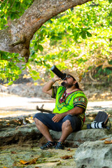 Local Costa Rican man in a Caribbean shirt drinking water by the Caribbean Sea on a beach in...