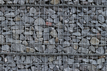 Rubble stone in galvanized mesh. Background. Gabion mattress made of woven mesh with stones for creating walls. Stones in mesh, creating decorative walls, strengthening
