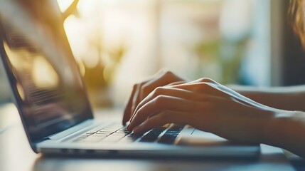 Photograph of a person typing on a laptop, bathed in warm sunlight, with blurred greenery in the background.