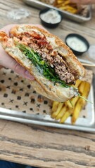 A juicy beef burger with fresh greens and sauce held in hand, with crispy french fries in the background. The image represents delicious fast food and casual dining enjoyment