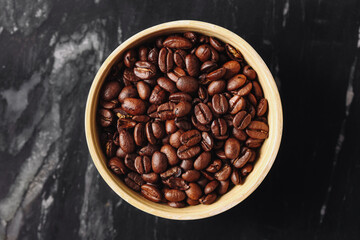 Roasted coffee beans in bowl. Brown aromatic grains on black marble. Fresh caffeine source. Natural organic drink ingredient. Morning energy concept. Minimal food flatlay for coffee lovers.