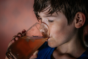 Close-up of a boy with piercing eyes drinking iced tea from a glass, with dramatic lighting and...