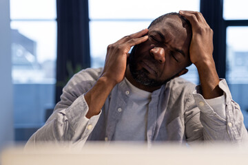 African american man at the laptop looking tired and suffering from a headache