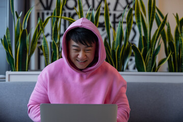 Asian young man in a pink hoodie at the laptop