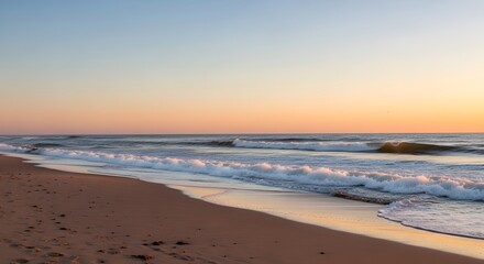 Scenic coastal landscape at dawn with gentle waves rolling onto the sandy beach under a pastel sky reflecting warm light of the setting sun.