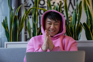 Asian young man in a pink hoodie at the laptop looking happy