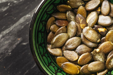 Obraz premium Roasted pumpkin seeds in bowl. Healthy snack on marble background. Natural vegan food rich in fiber. Tasty dietary ingredient. Closeup of organic superfood. Nutrition concept for clean eating.